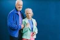 Senior couple posing confidently in stylish outfits against a blue backdrop.